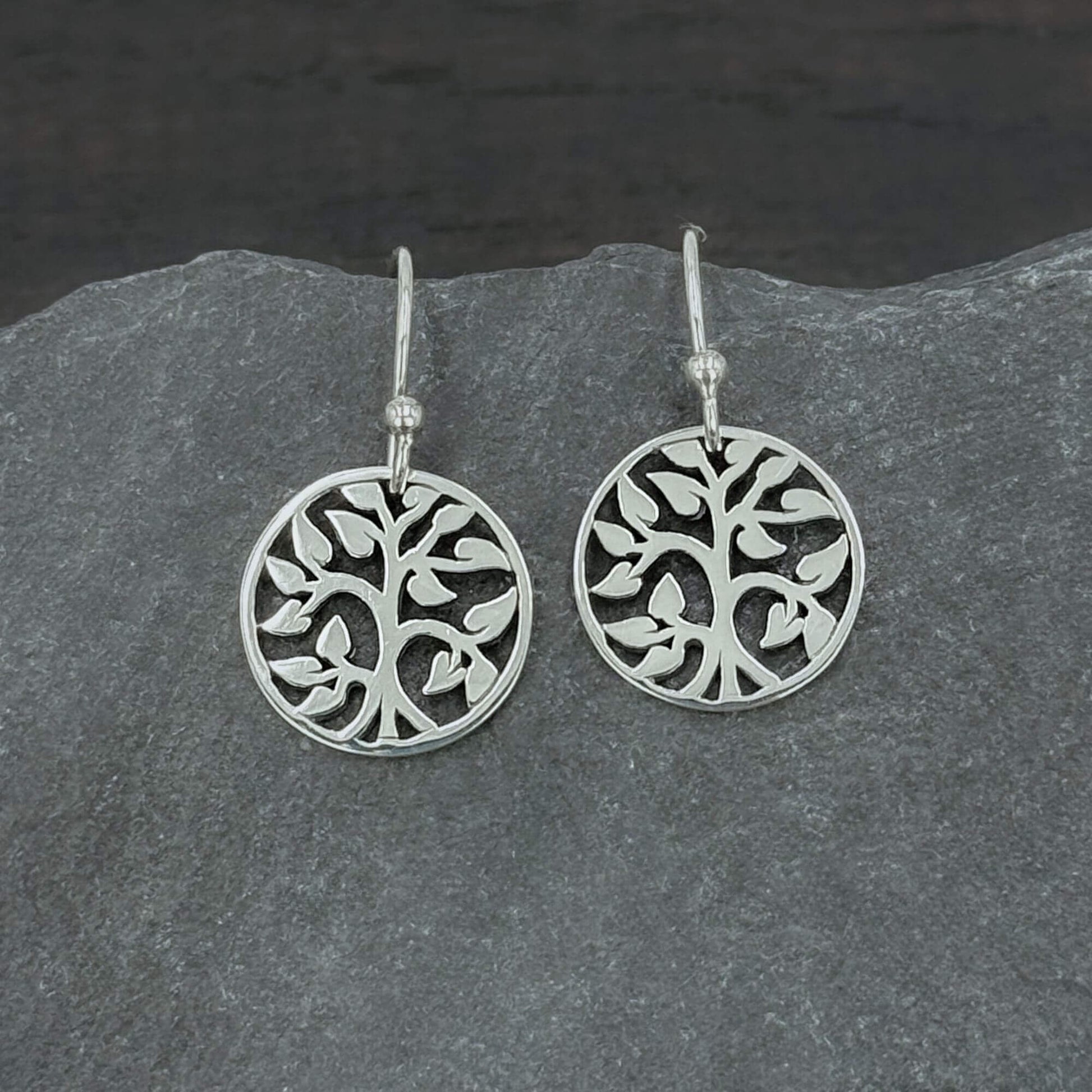 Close up view of 925 solid sterling silver earrings dangling from hook earwires with small circular Tree of Life charms with an openwork cut out design.  The tree charms are 5/8" tall and dangle freely.  A perfect jewelry gift for nature lovers.