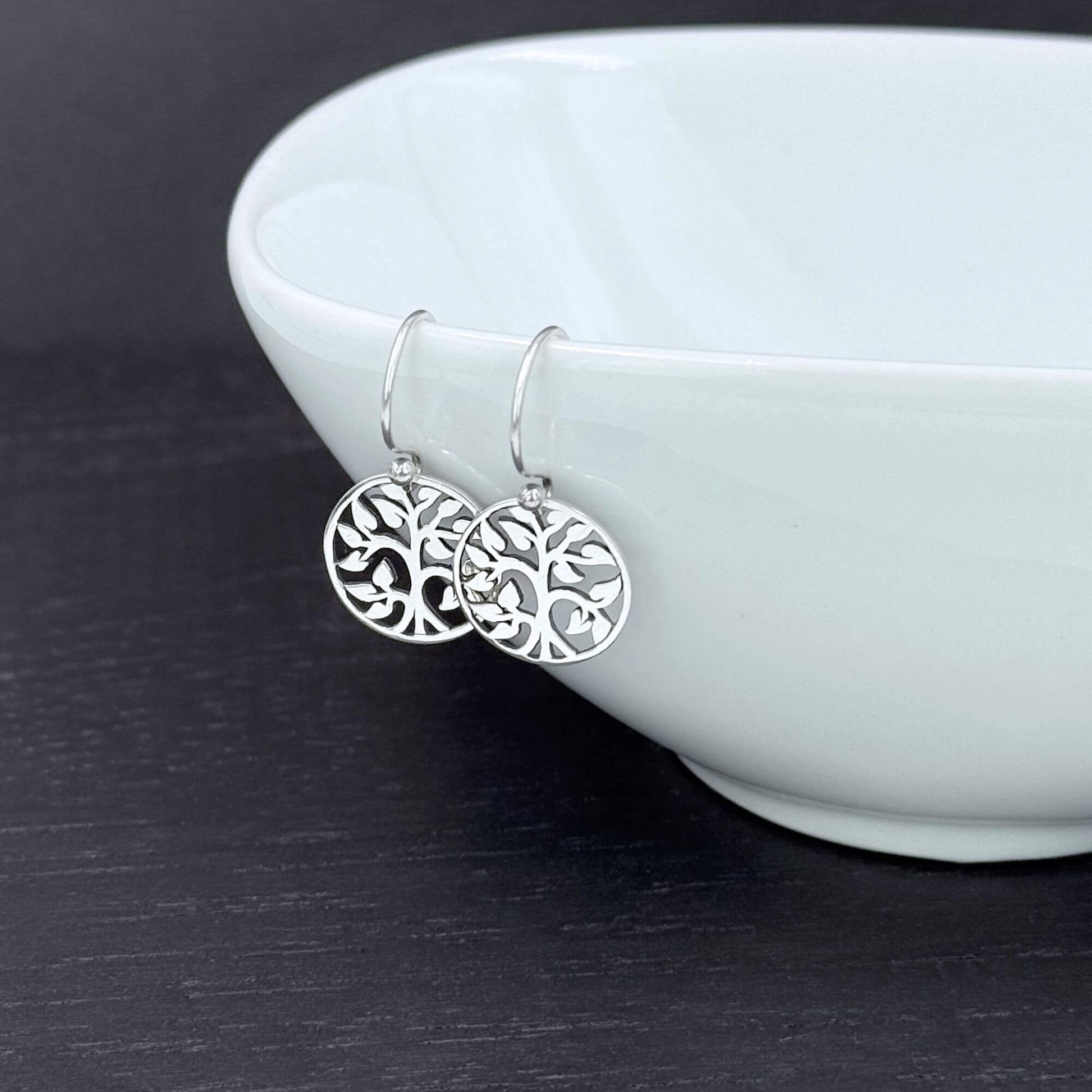 CLose up of shiny small round tree earrings for women with a cut out design.