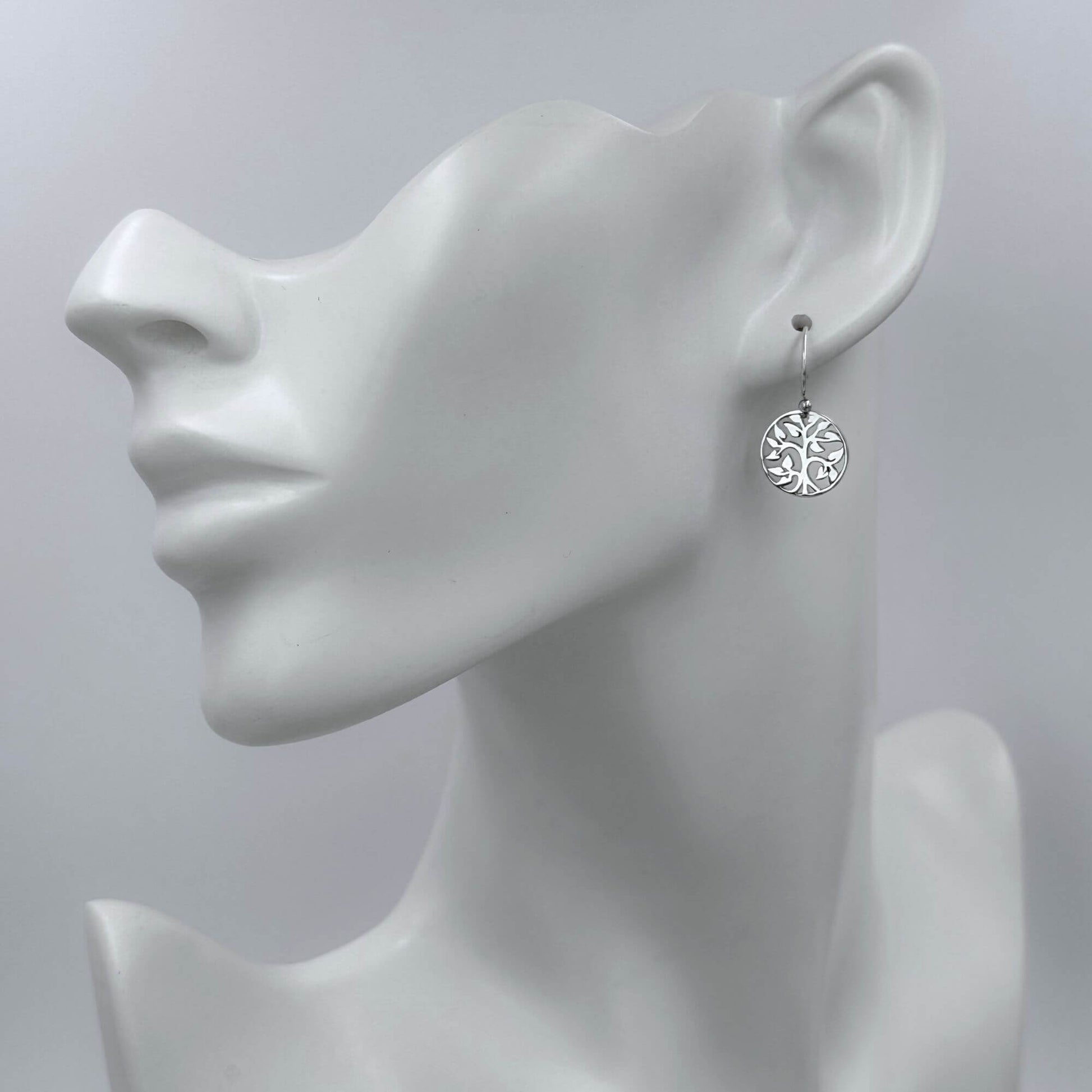 A woman wearing 925 solid sterling silver earrings with circle tree charms dangling from 925 solid sterling silver hook earwires. 