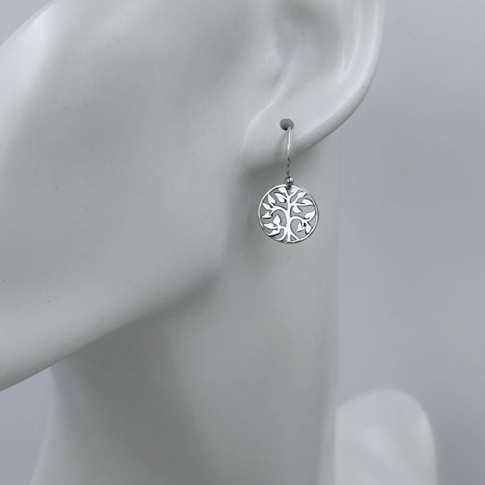 Macro view of a womans earlobe with a small round tree charm earring on a hook earwire. 