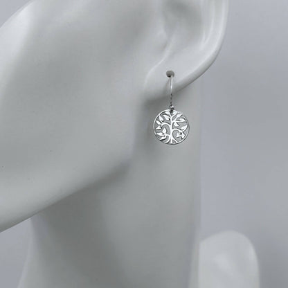 Macro view of a womans earlobe with a small round tree charm earring on a hook earwire. 