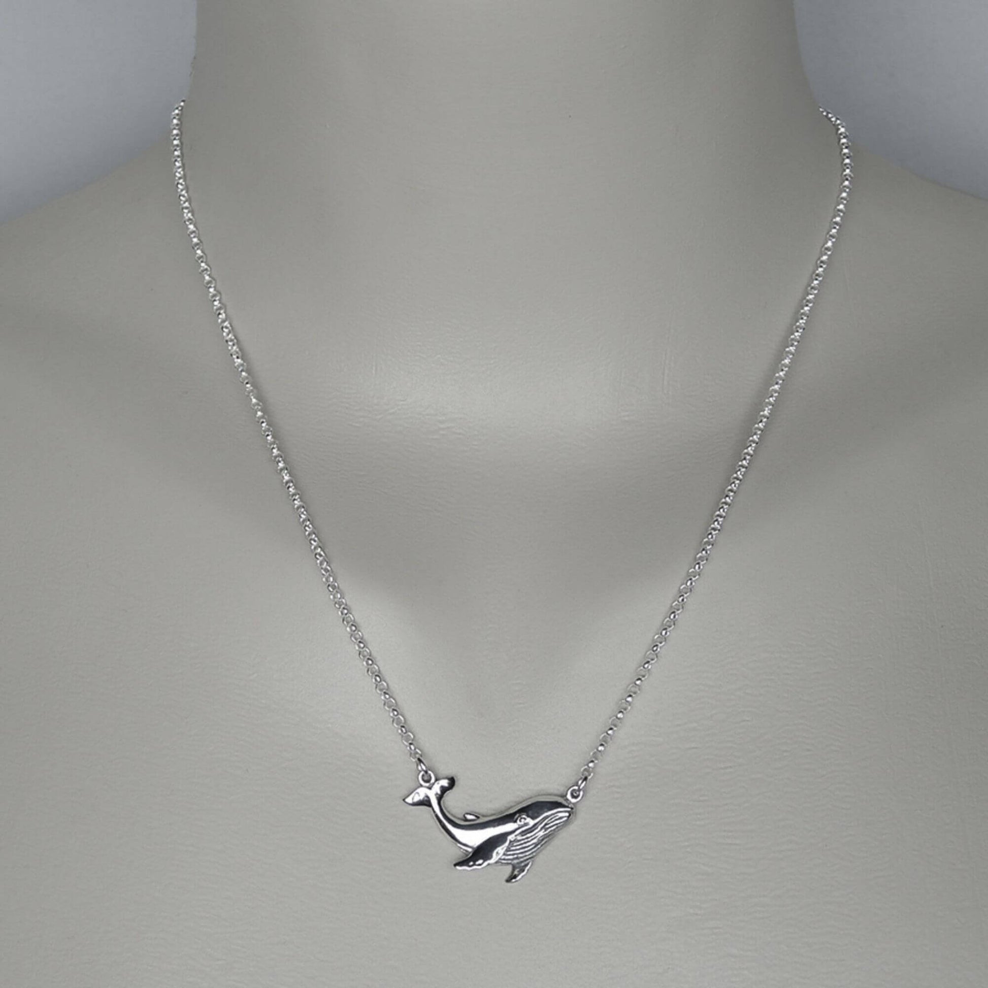 A woman wearing a sterling silver chain necklace with a silver whale necklace